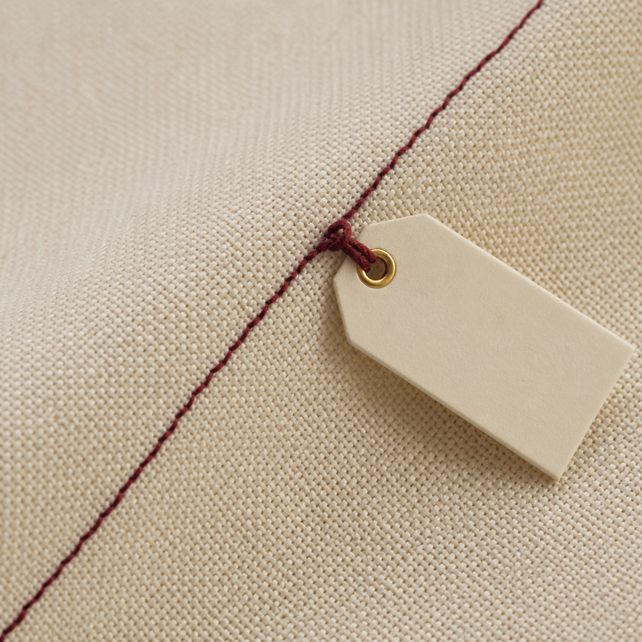 Primo piano di tessuto color crema con cucitura bordeaux e cartellino in carta.